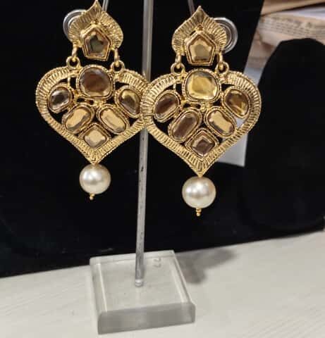 The earrings shown in the image are a style of traditional Indian jewelry known as Kundan or Polki earrings, often featuring a design with a pearl drop