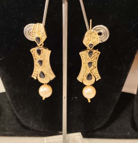 This is a pair of traditional Indian earrings with a gold-toned finish, black stones, and a pearl drop.